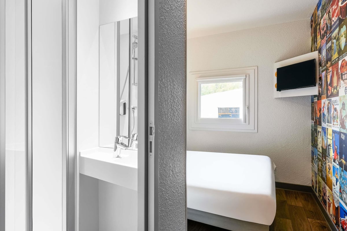 Een moderne badkamer met een douche, toilet en wastafel. Er is een raam dat voor daglicht zorgt en een aan de muur bevestigde televisie.