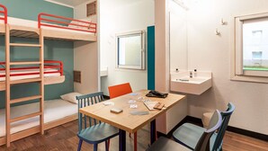 Quarto com beliches, uma mesa e cadeiras, uma janela e um pequeno armário com produtos de higiene pessoal.