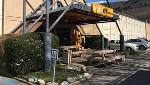 A hotel entrance with a covered outdoor area, picnic tables, and a disabled parking sign. - hotelF1 Annemasse (Saint-Cergues)