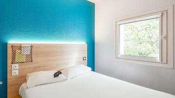 Quarto de hotel com cabeceira de madeira, cama branca, janela com vista para o verde e parede decorada em azul.