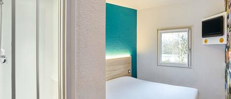 Une chambre d’hôtel avec un lit, une fenêtre, une télévision et un espace douche.