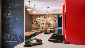 L’intérieur d’un restaurant avec un mur recouvert d’un tableau noir, des tables, des chaises et un mur orné d’affiches colorées.