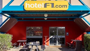 Una entrada de hotel moderna con fachada roja, asientos exteriores y un cartel que dice hotelF1.com.