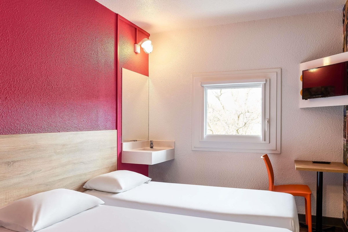 Una habitación de hotel con cama, ventana, escritorio y una silla.