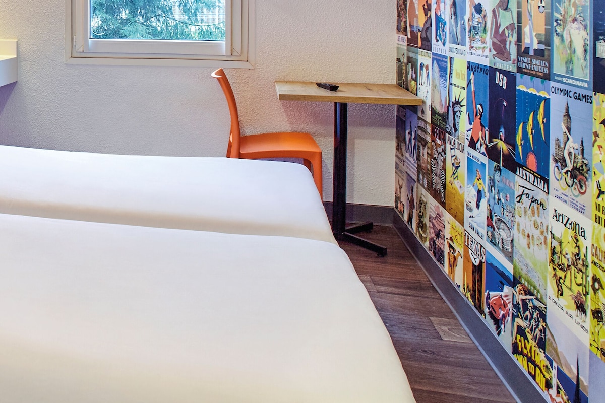 Une chambre d’hôtel avec un lit, un lavabo, une chaise et un mur décoré de posters.