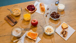 Una mesa de madera con alimentos para el desayuno, como tostadas, cereales, fruta y bebidas.