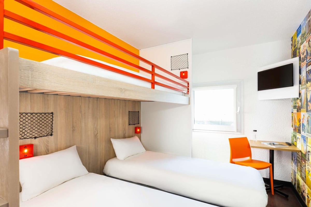 Une chambre avec un lit superposé, un bureau et une chaise, une télévision et un mur décoré de tableaux.