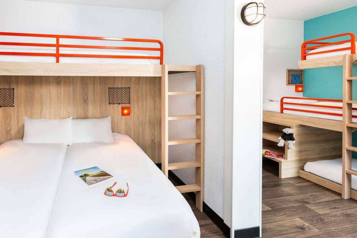 Ein Zimmer mit Etagenbetten, einem Holzkopfteil, einem Regal mit einem Teddybären und einer wandmontierten Leuchte.