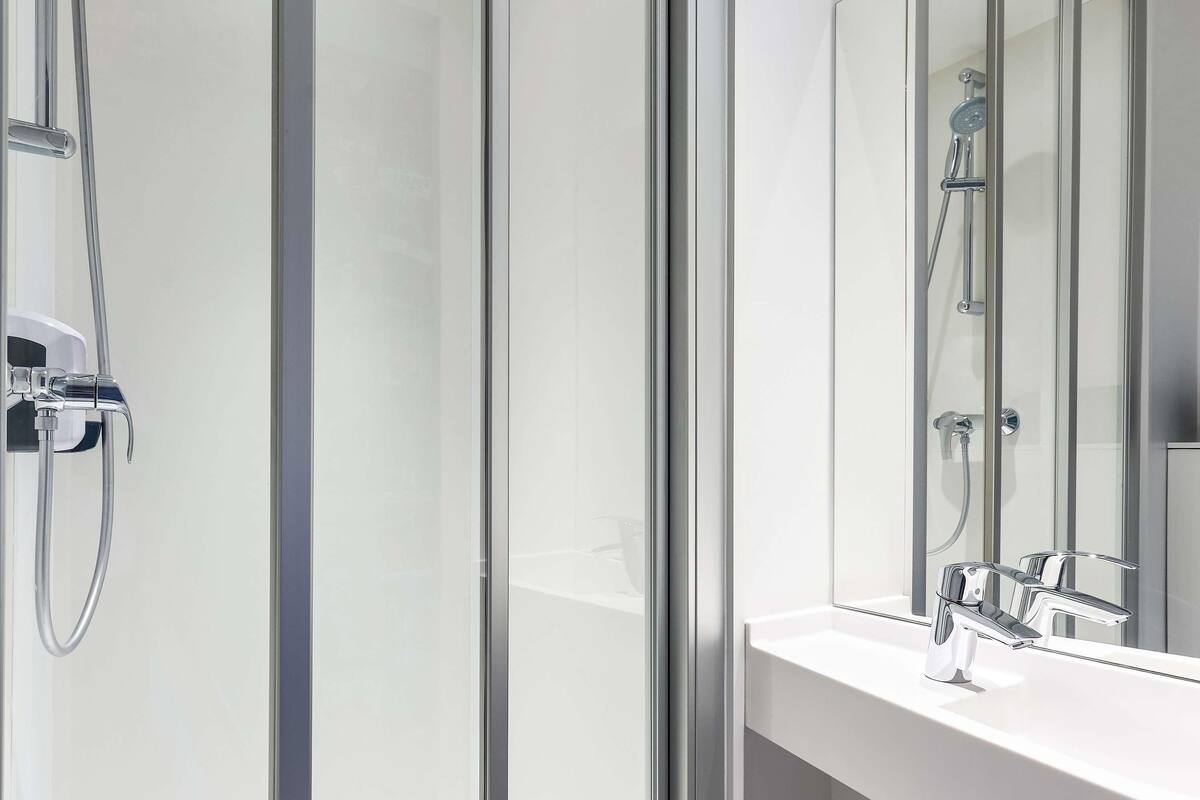 A modern bathroom with a glass shower enclosure, a white sink, and a large mirror.