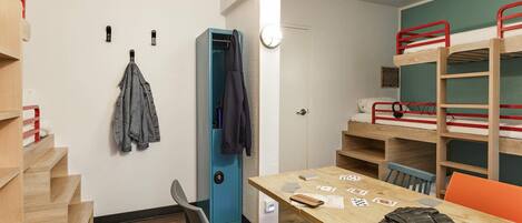 A dormitory room with bunk beds, a desk with cards, a chair, and a coat rack.