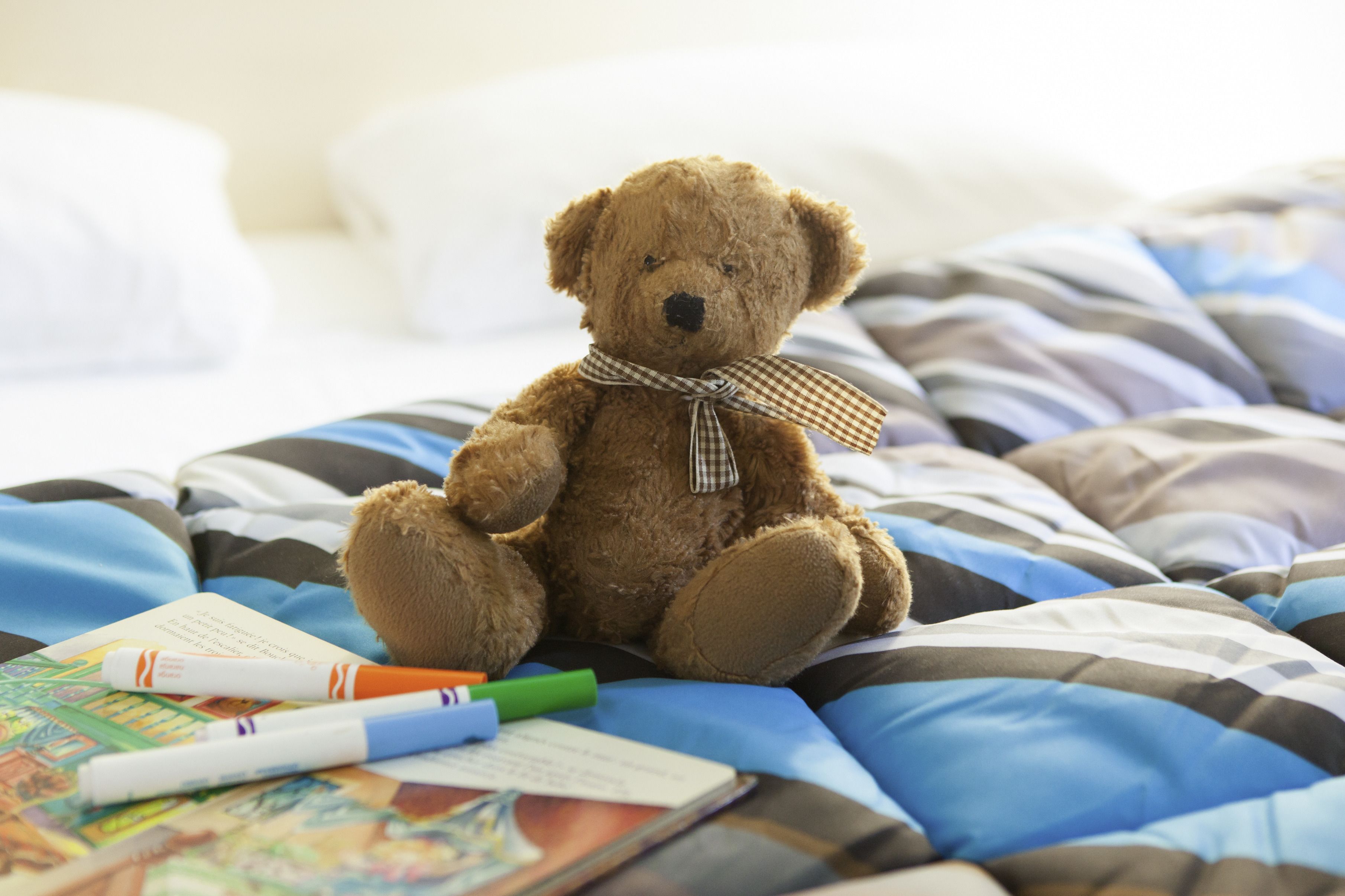 A teddy bear sitting on a bed with striped bedding and a book.
