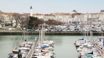 Un port de plaisance où sont amarrés de nombreux bateaux, une statue et un phare en arrière-plan.