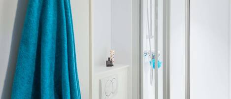 A bathroom with a glass shower enclosure, a towel rack with a blue towel, and a small shelf with toiletries.