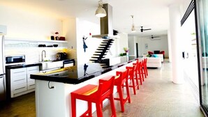 A modern kitchen with a central island, red bar stools, and a dining area with a white sofa. - The Marion Villa (Scarborough)