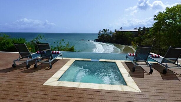 A wooden deck with a hot tub and lounge chairs facing a beach with waves. - The Marion Villa (Scarborough)