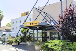 A hotel entrance with a modern design, a sign for 'Chambres Duo / Trio', and a website address 'hotelF1.com'.