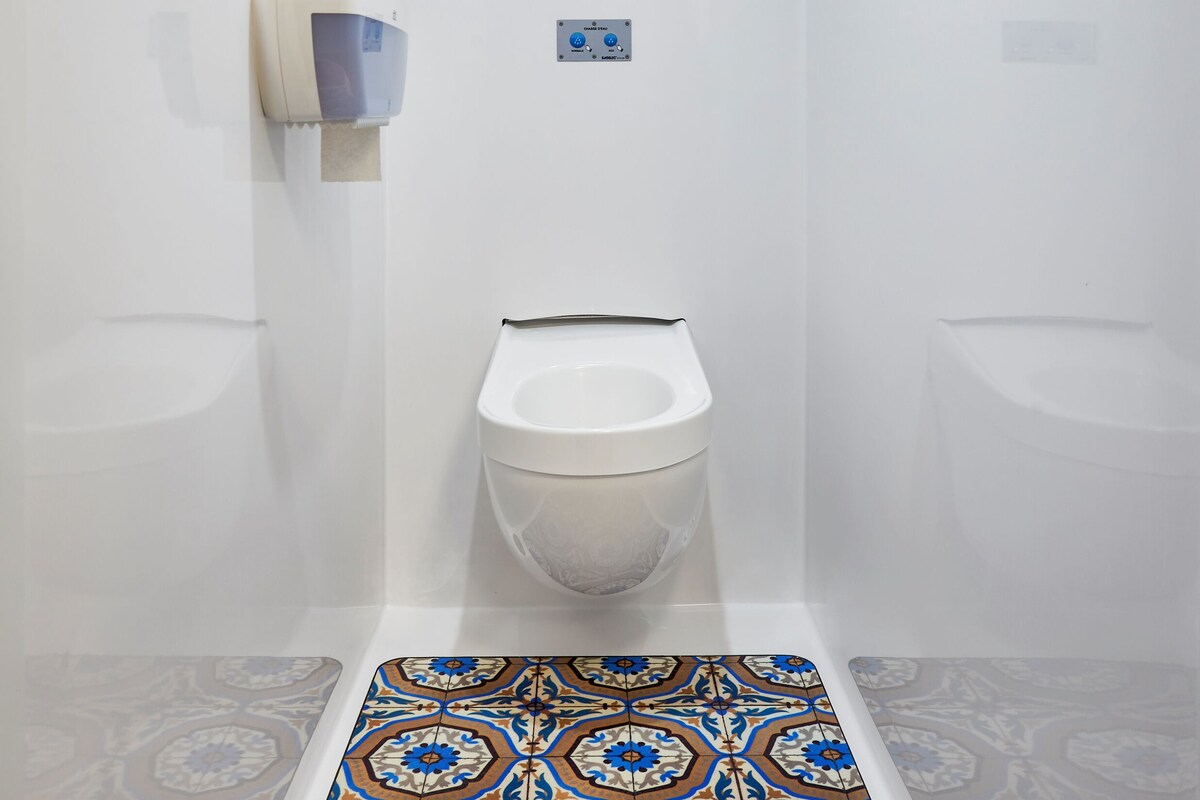 A small, modern bathroom with a toilet, a hand dryer, and a patterned floor.