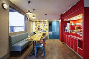 A dining area with a long wooden table, blue chairs, and a bench. There are blue cabinets and a red counter with a coffee machine.