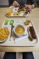 A breakfast tray with a cup of coffee, a chocolate spread on toast, a glass of orange juice, and a bowl of cereal.