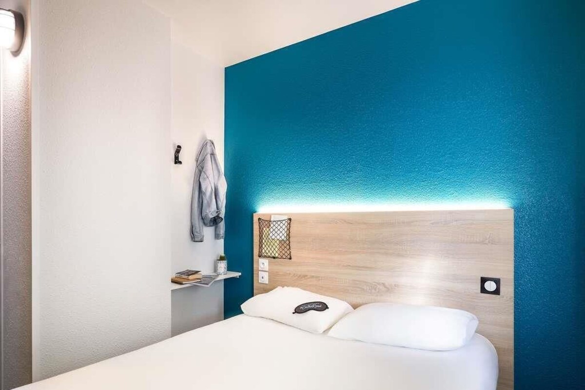 A hotel room with a bed, a nightstand, a wall-mounted shelf, and a blue accent wall.