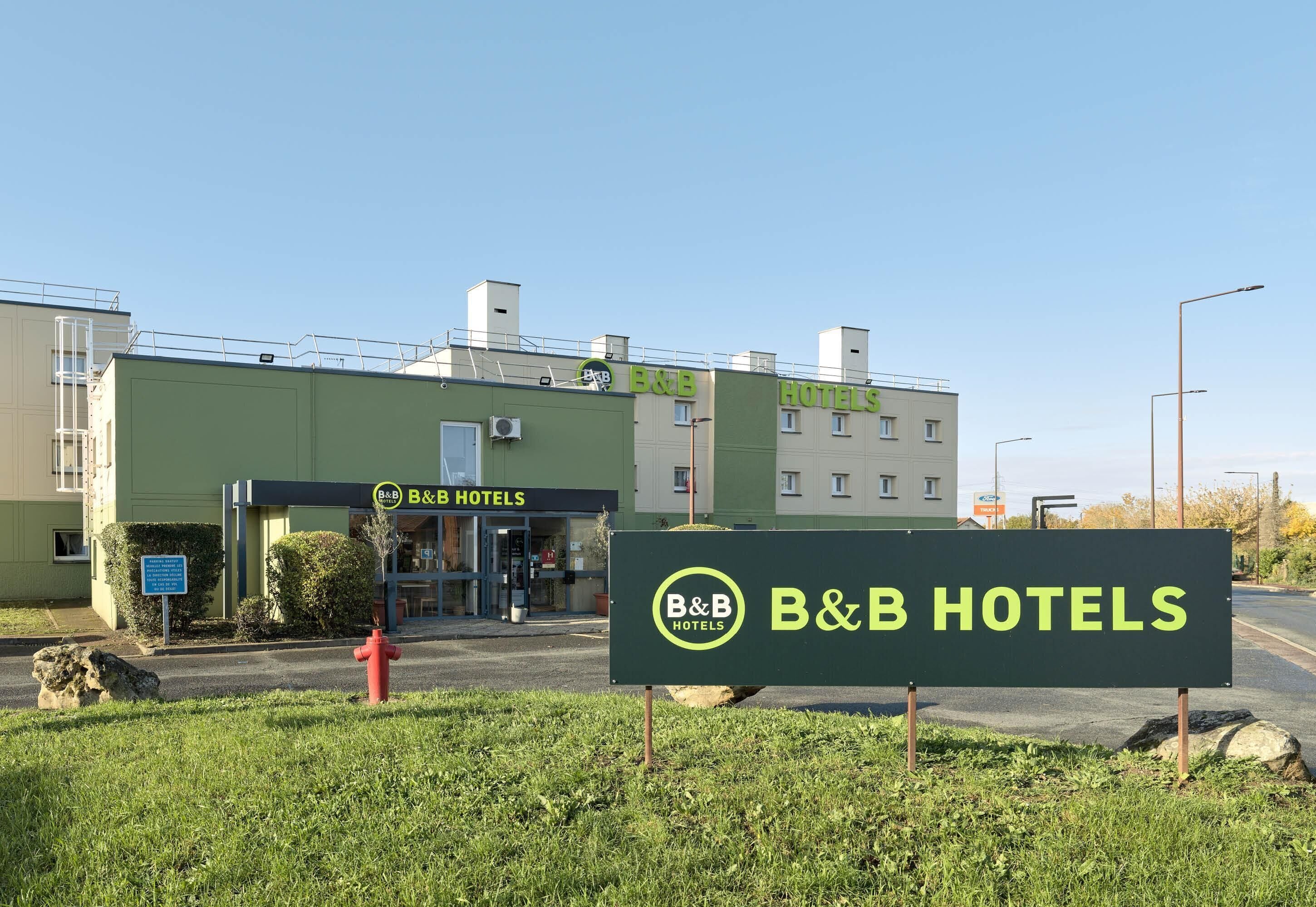 A B&B hotel with a green facade, a visible entrance, and a clear sky.
