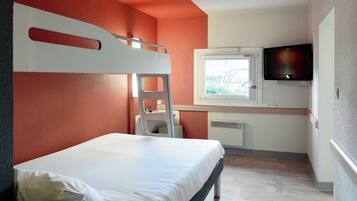A bunk bed with a white mattress and a ladder, a small desk with a chair, a television mounted on the wall, and a window with a view of greenery.