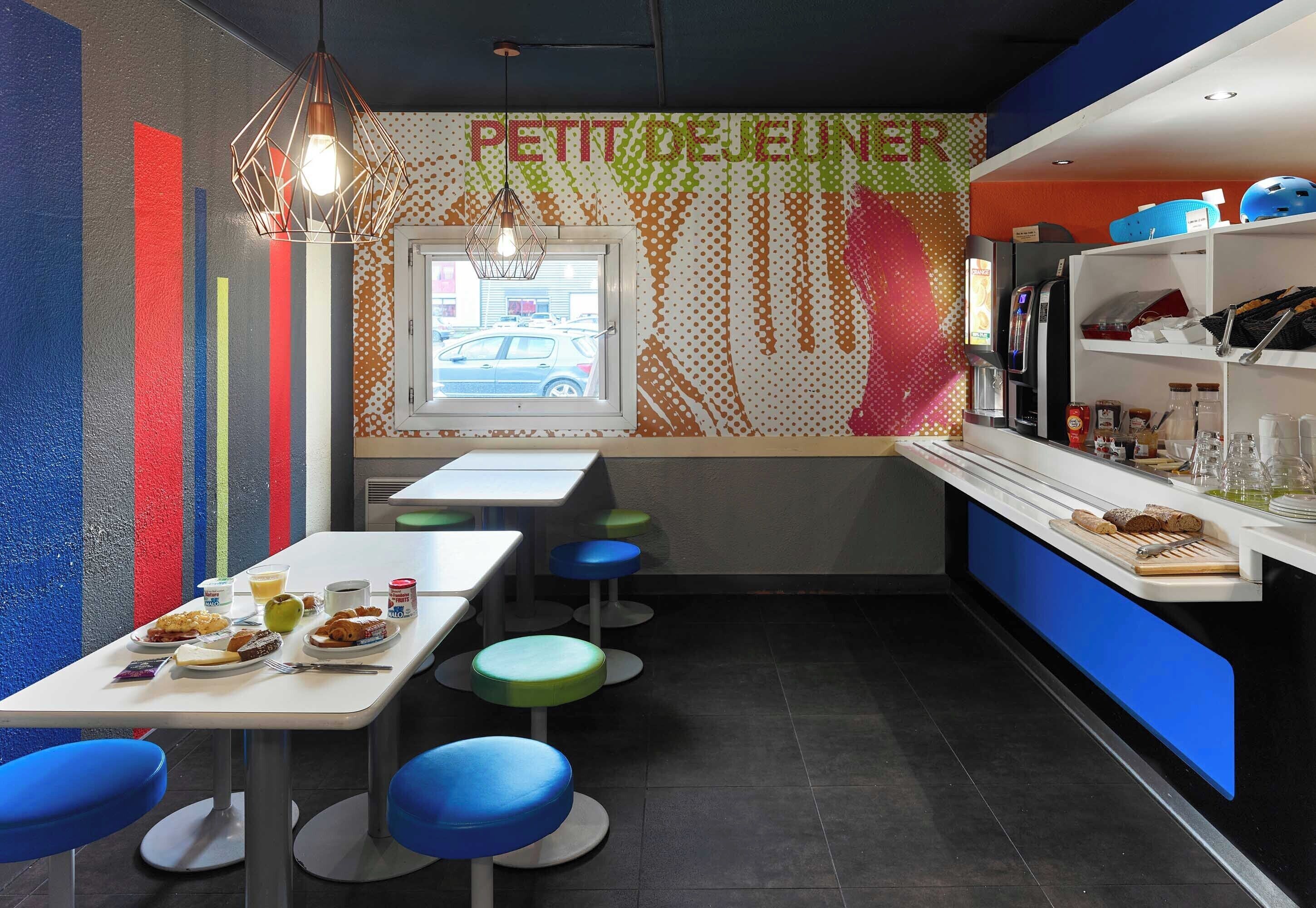 A modern café interior with colorful walls, a counter with beverages and snacks, and a window with a view of the street.