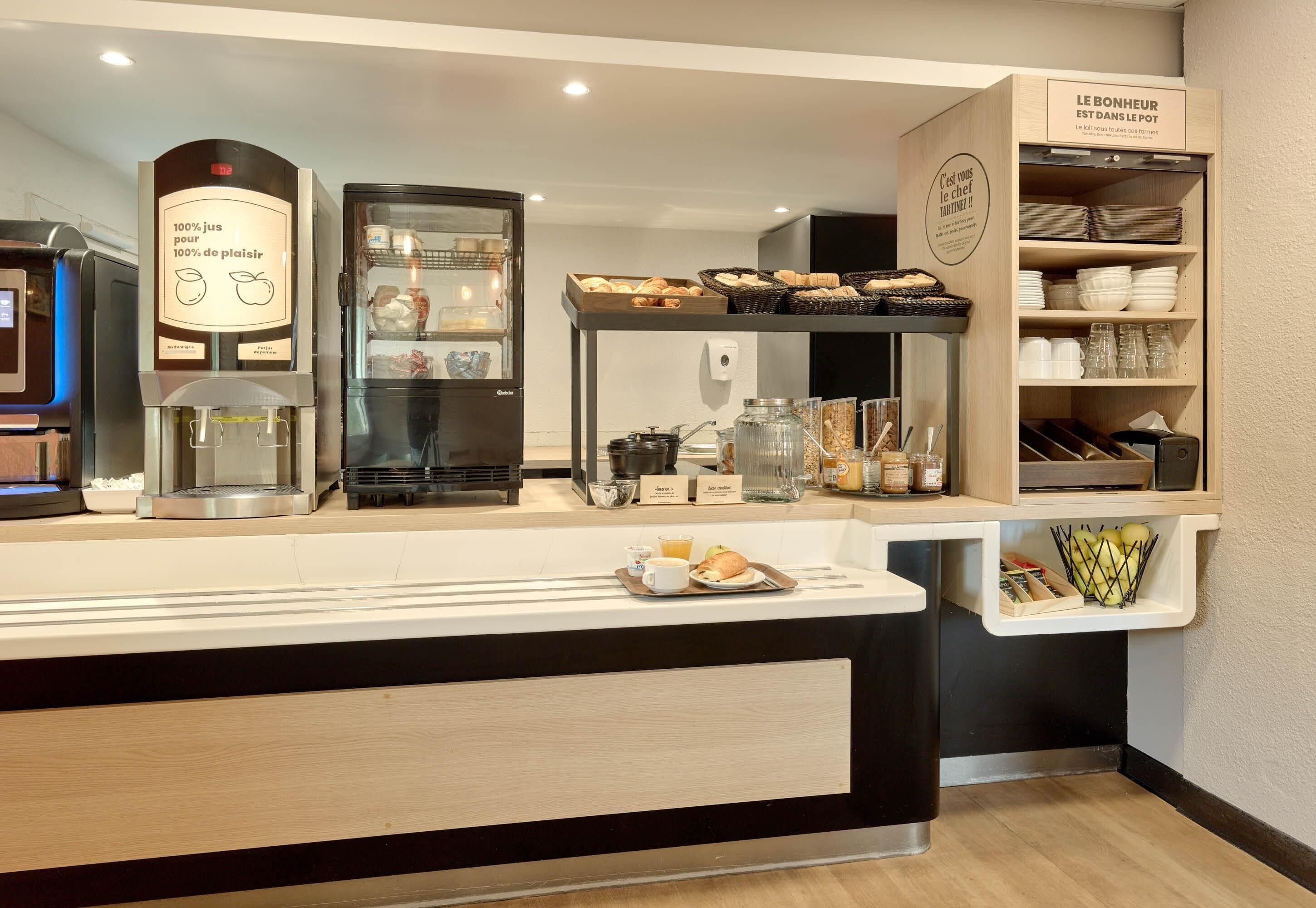 A breakfast bar with a coffee machine, a refrigerator, and shelves with bread and condiments.