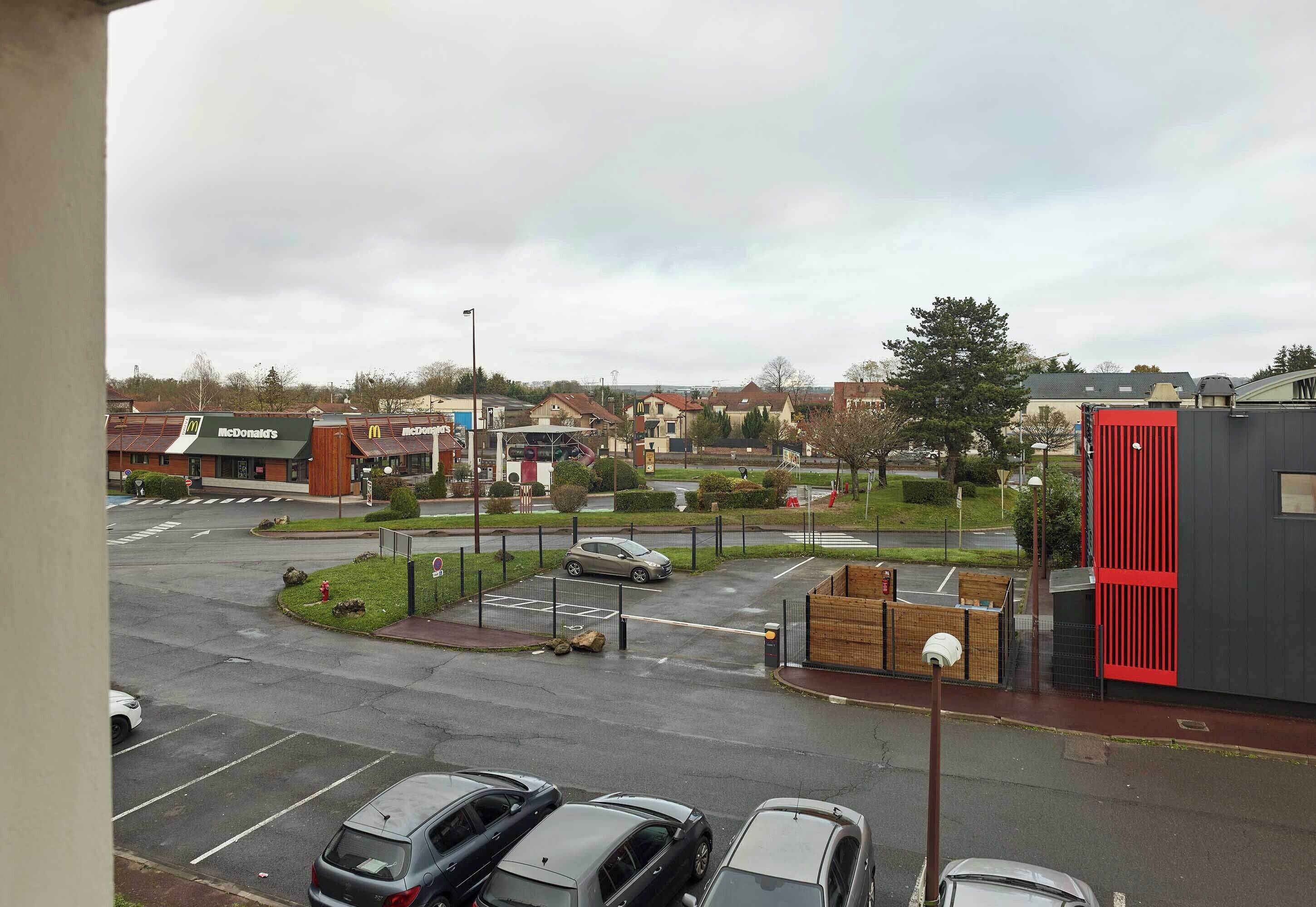 Un parking avec plusieurs voitures, un restaurant McDonald's et un bâtiment moderne agrémenté d’une touche de rouge.
