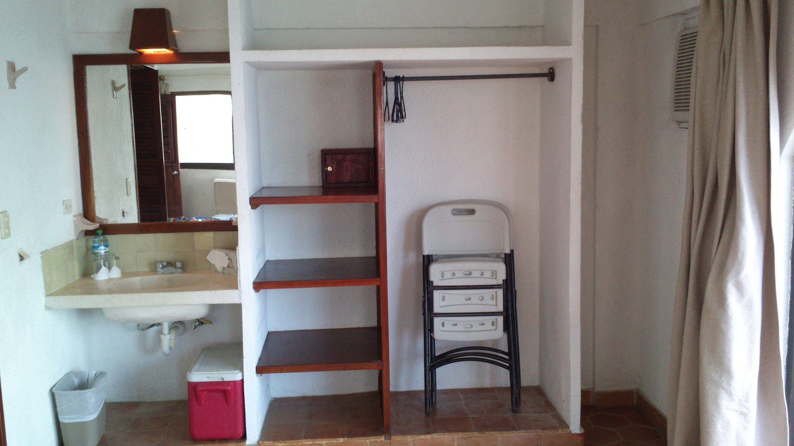 A compact bathroom with a sink, mirror, and a small shelf unit.