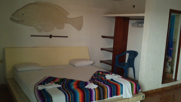 Un dormitorio con una cama, una manta colorida, un mural de peces, una silla azul y un estante de madera.