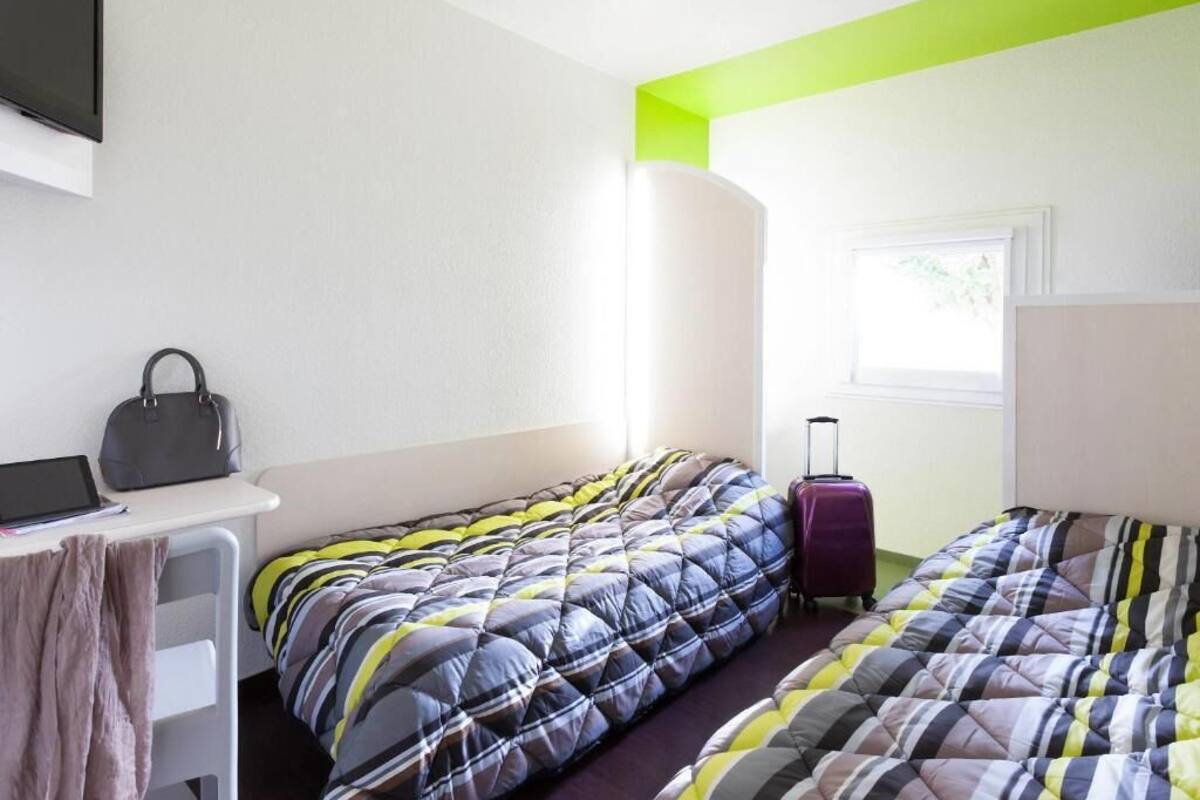 A hotel room with two beds, a desk, a chair, a suitcase, and a TV.