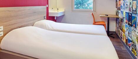 A hotel room with a wooden headboard, a white bed, a small sink, an orange chair, and a wall decorated with travel posters.