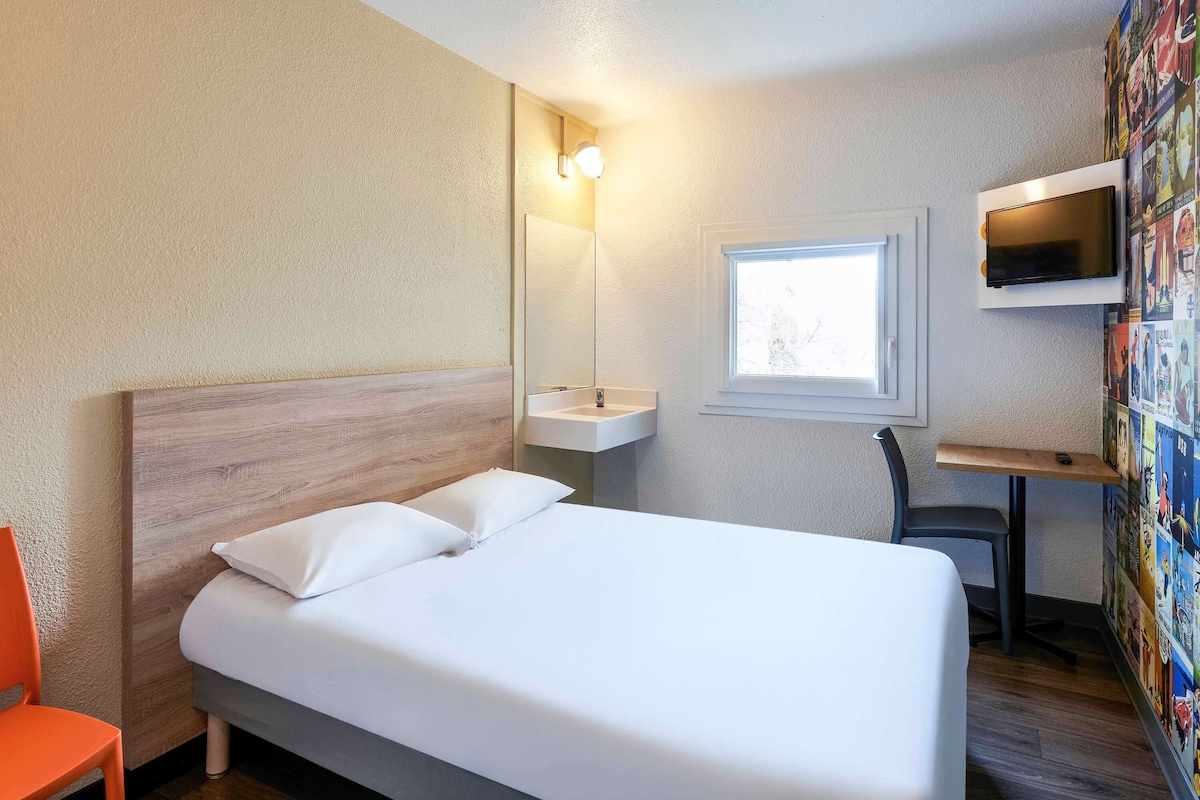 Une chambre d’hôtel avec un lit, un bureau, une chaise, une télévision et une fenêtre.