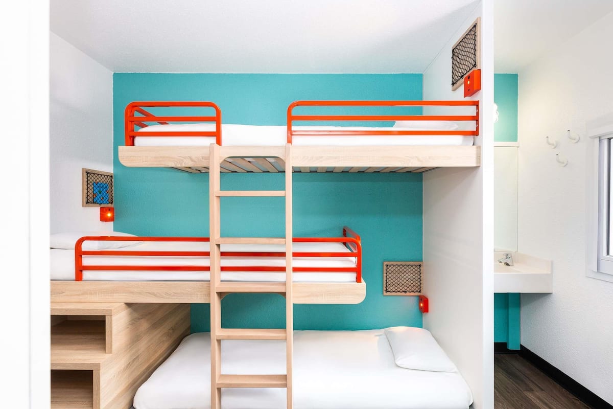 A bunk bed room with a wooden ladder, a small window, and a sink.