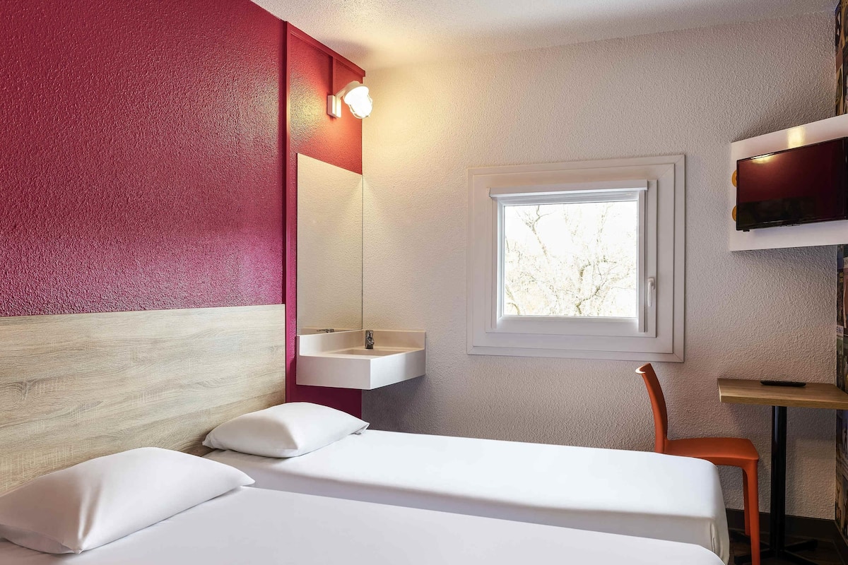 A hotel room with a bed, a window, a sink, and a television.
