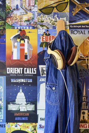 A denim jacket with headphones hanging on a wall with various travel posters. - hotelF1 St Witz A1 Paris Nord (Saint-Witz)