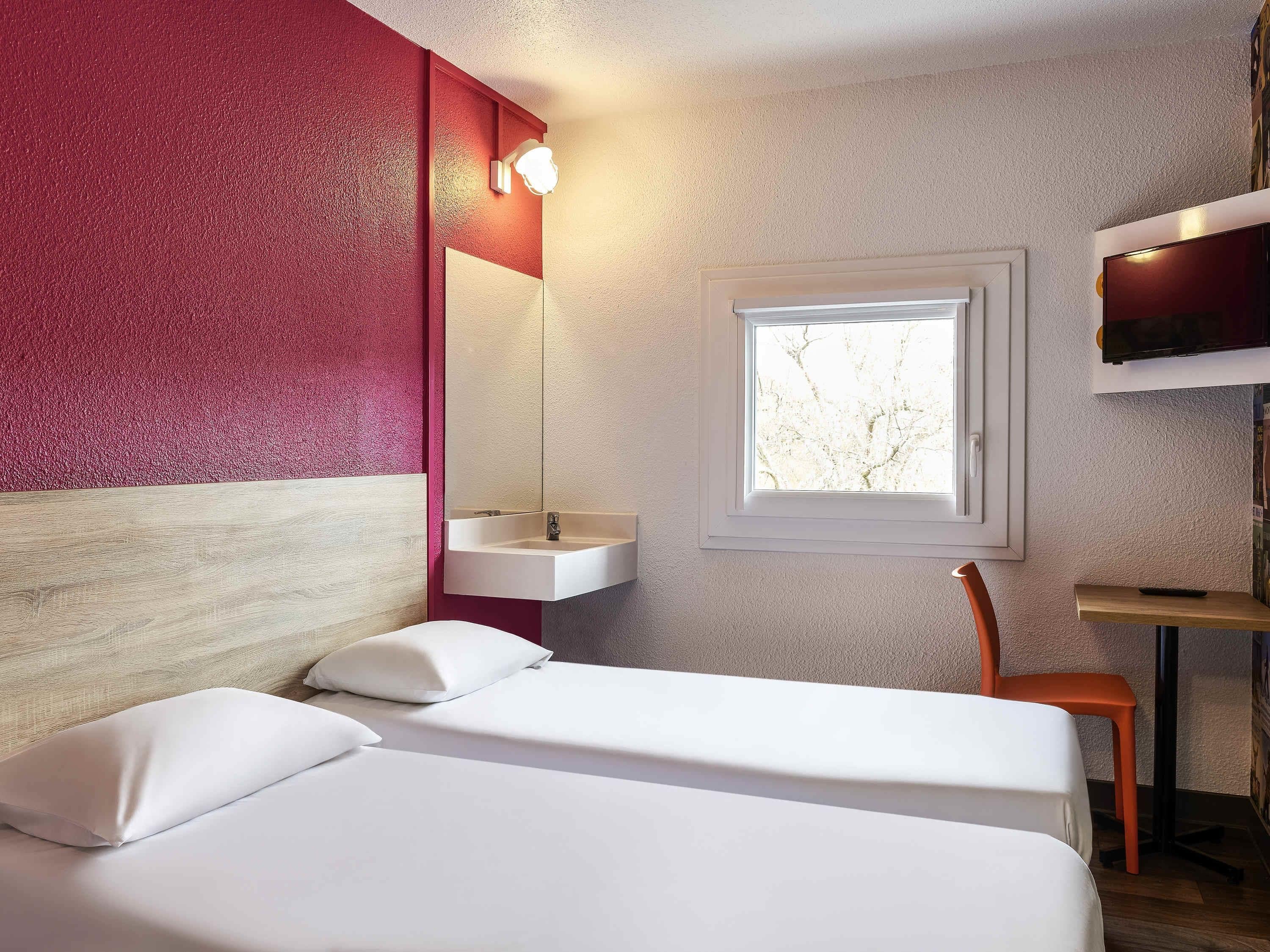 Une chambre d’hôtel avec un lit, une fenêtre, un lavabo et une télévision.