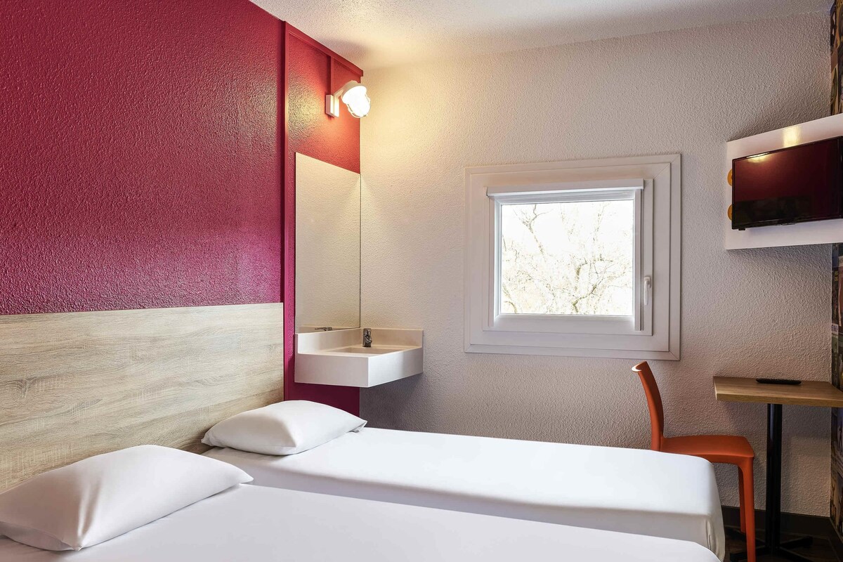 A hotel room with a bed, a window, a sink, and a TV.