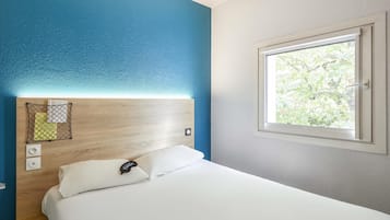 Een hotelkamer met een bed, een hoofdeinde met een plank, een raam met uitzicht en een stopcontact.