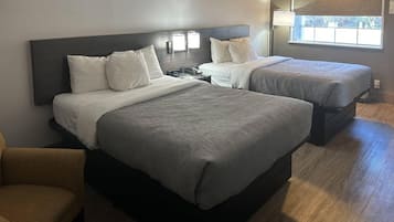 Habitación de hotel con dos camas, una mesita de noche, una silla y una ventana con persianas.