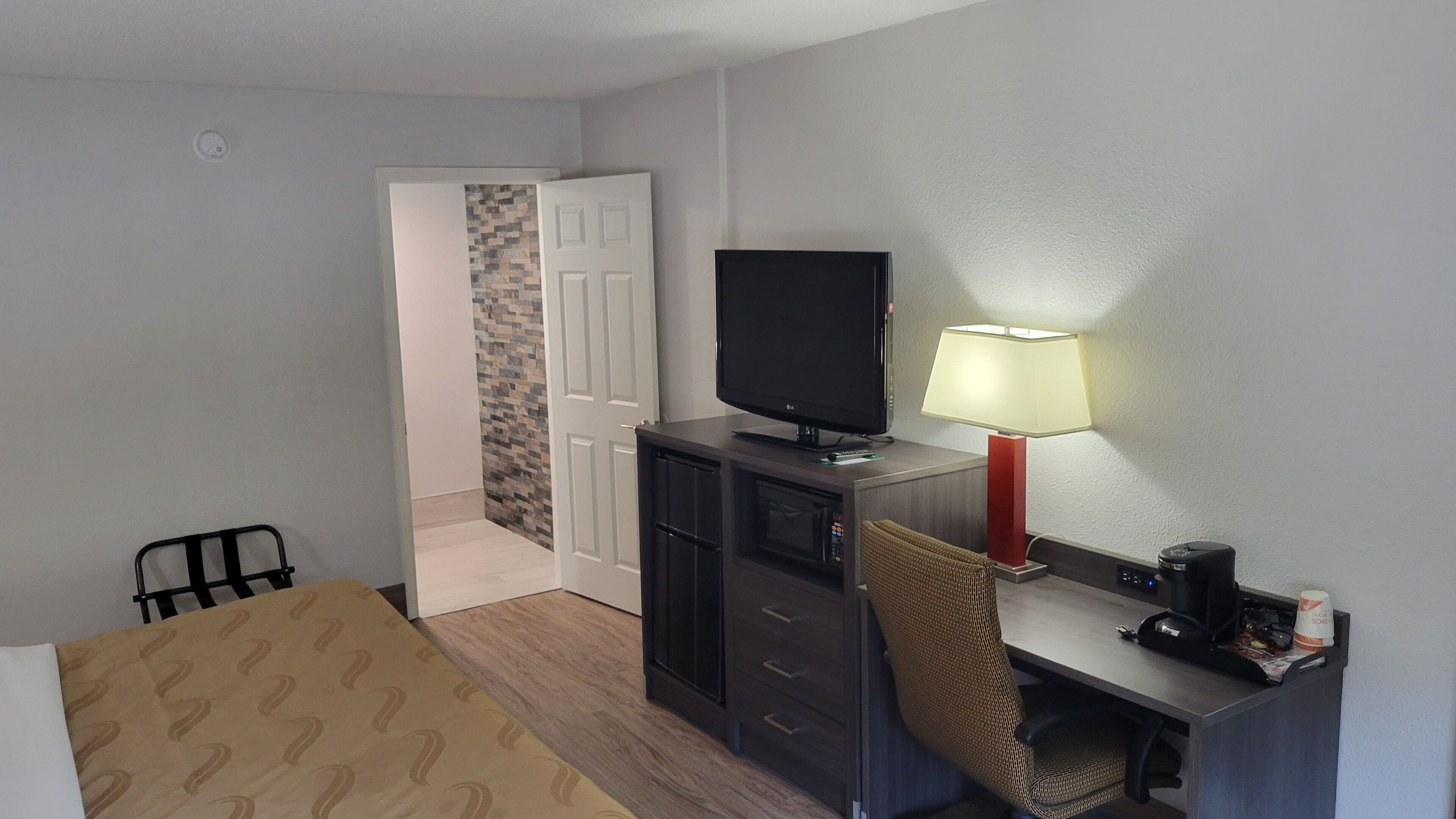 Hotellihuone, jossa on sänky, työpöytä lampun kanssa, televisio ja tuoli.