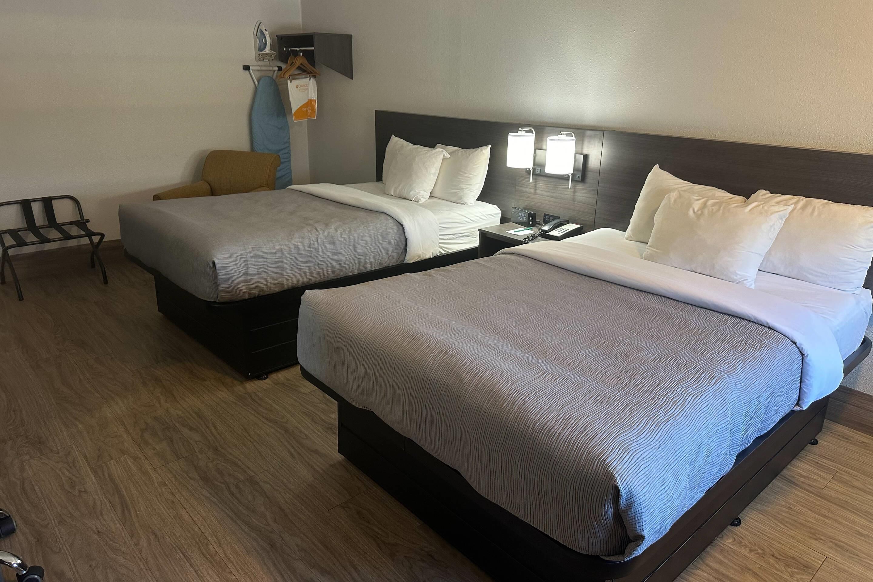 A hotel room with two beds, a chair, a coat rack, and a bedside table with a phone.