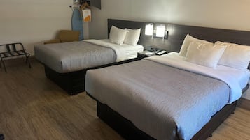 A hotel room with two beds, a chair, a coat rack, and a bedside table with a phone.