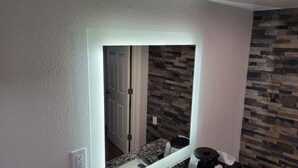 A bathroom with a large mirror, a granite countertop, and a tiled wall.
