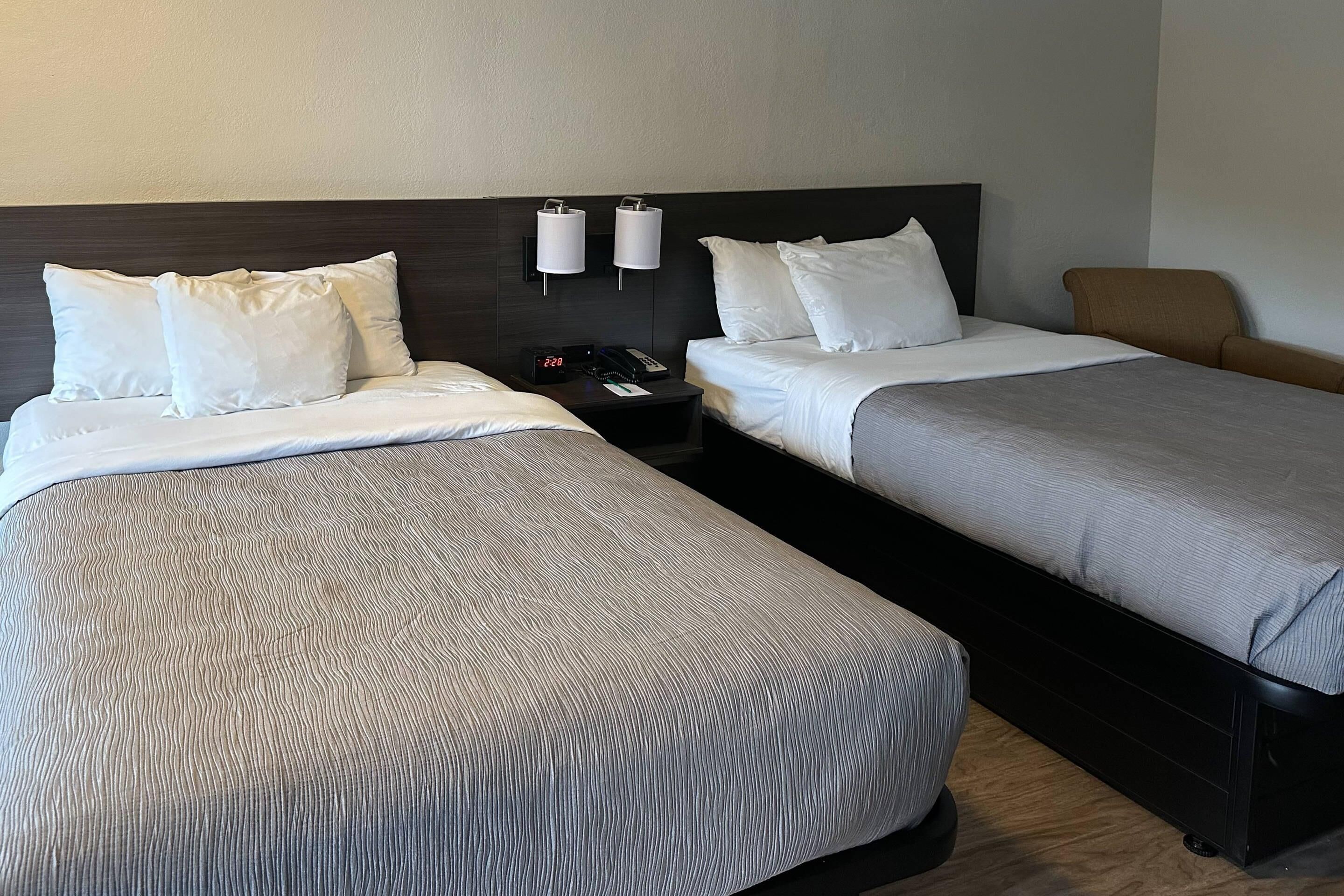 Une chambre d’hôtel avec deux lits, une table de chevet avec un téléphone et une horloge, et une chaise.