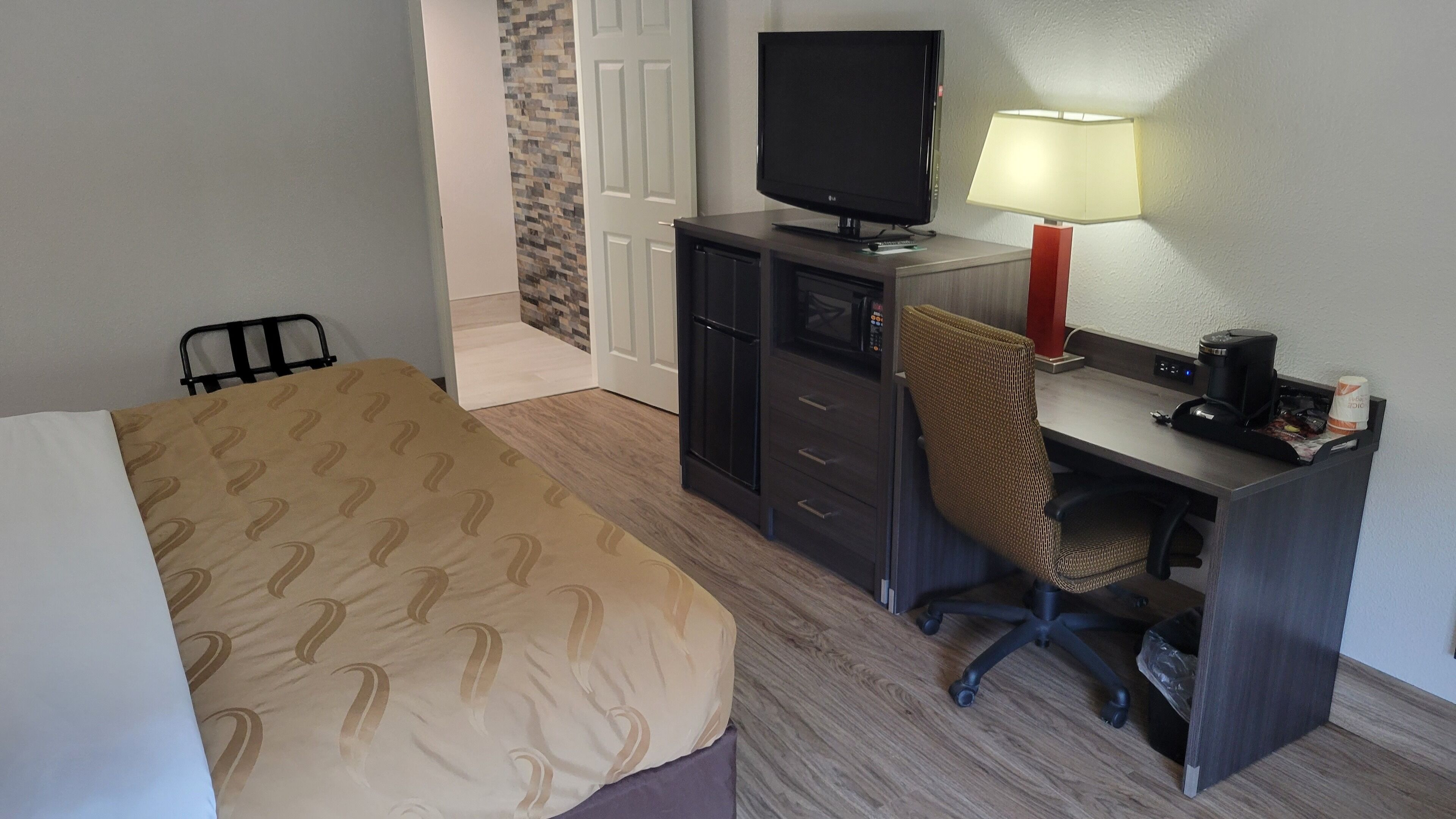 Habitación de hotel con una cama, un escritorio con computadora, una silla, un televisor y una lámpara.