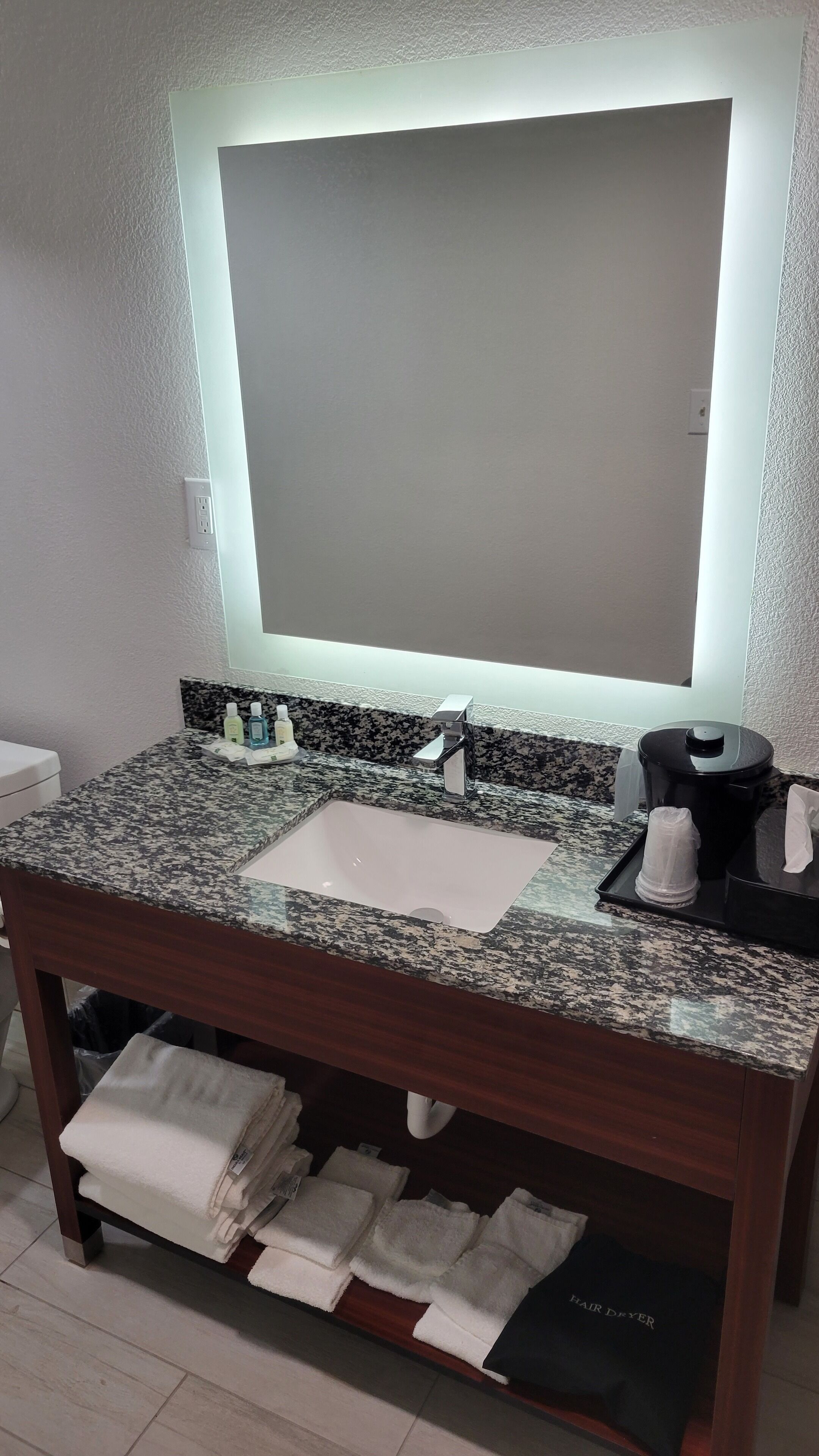 A bathroom with a granite countertop, a sink, a mirror, and a towel rack with folded towels.