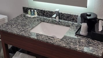 A bathroom with a granite countertop, a sink, a mirror, and a towel rack with folded towels.