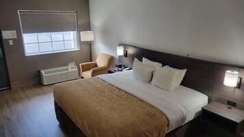 Habitación de hotel con una cama grande, una silla, una mesita de noche con lámpara, un calentador y una ventana con persianas.